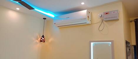 A room with a ceiling-mounted air conditioner, a wall-mounted thermostat, and a hanging pendant light.