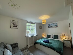 A bedroom with a bed, a window, a radiator, a wall-mounted picture, and a bedside table with a lamp. - Gorgeous 3 Bedroom Cottage In Canterbury (Canterbury)