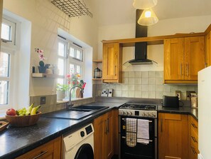 A kitchen with wooden cabinets, a built-in washing machine, a stove, and a sink. - Gorgeous 3 Bedroom Cottage In Canterbury (Canterbury)