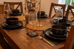 A wooden dining table set with black plates, bowls, and a clear glass. - Gorgeous 3 Bedroom Cottage In Canterbury (Canterbury)