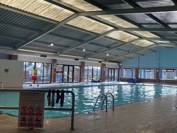 An indoor swimming pool with a roof, a pool user’s guide sign, and a view of the outside. - Charming Lodge Retreat With Garden View (Dover)
