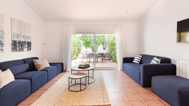 En moderne stue med to sofaer, et lille bord og udsigt til en udendørs terrasse gennem en glasdør.