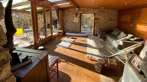 Interior acogedor de una cabaña con pared de piedra, techo de madera y un tragaluz grande.