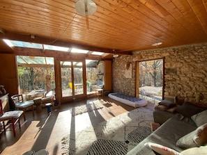 Ett rymligt rum med ett träpanelat tak, stora fönster, en vägg av sten och en mysig sittgrupp med en soffa och en bänk.