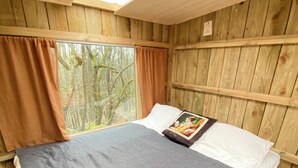 Una habitación de madera con cama, cortinas, una ventana y un tragaluz.