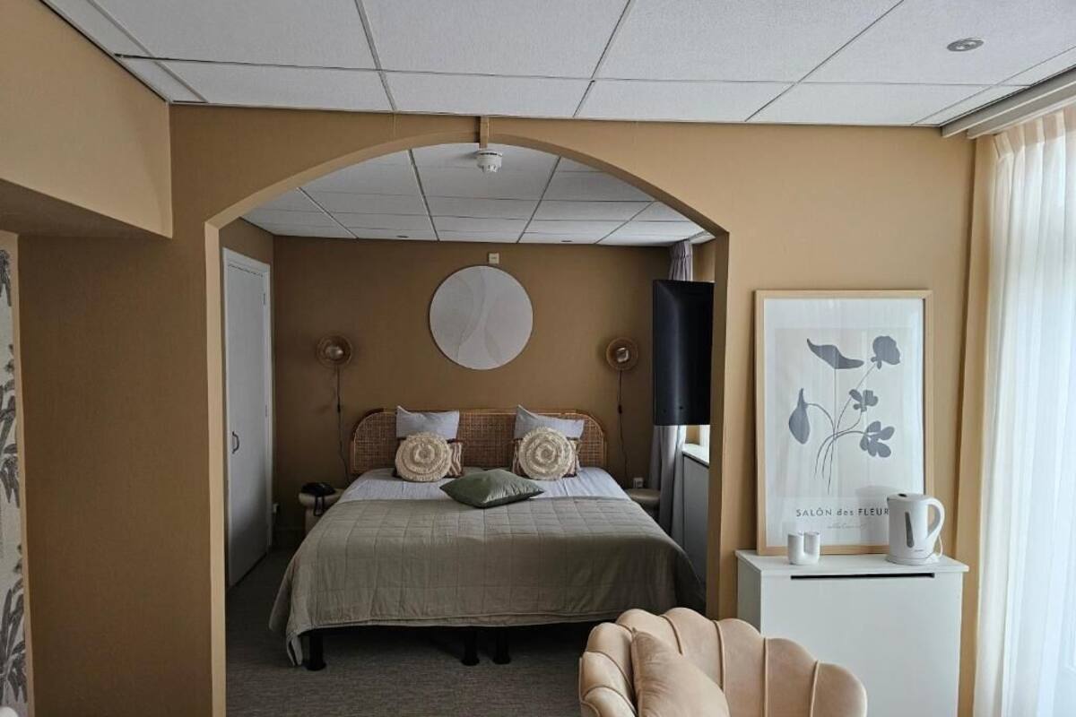 Una habitación de hotel con una cama, una silla, un televisor, un cuadro y una cafetera.