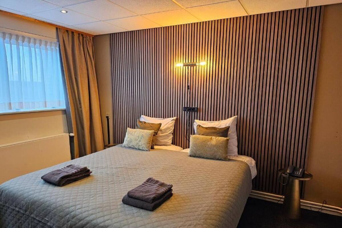 Habitación de hotel con una cama grande, dos mesitas de noche, una lámpara de pared y un radiador.