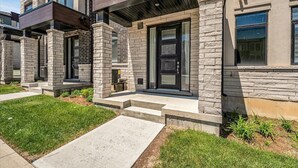 A modern townhouse with a stone facade, a front porch, and a visible garage door. - Brand New 4-BR Ensuite Townhouse | Netflix/Disney+ (Cambridge)