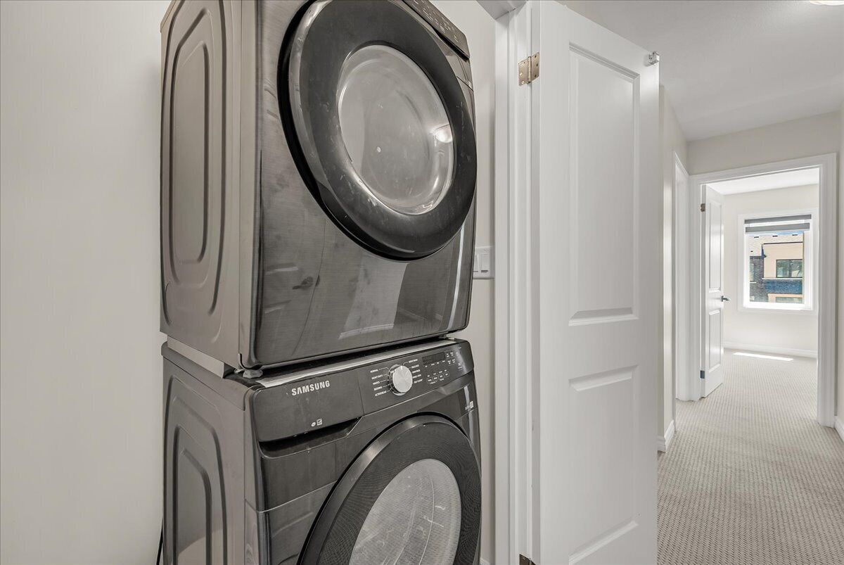 A stacked washer and dryer in a hallway with a door leading to another room.