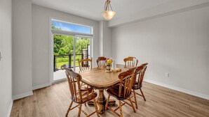 A dining area with a wooden table and chairs, a vase with flowers, and a view of greenery outside. - Brand New 4-BR Ensuite Townhouse | Netflix/Disney+ (Cambridge)