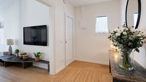 A modern living room with a flat-screen TV, a wooden bench, a small table with a vase of flowers, and a large mirror on the wall. - Rosari II - Detached House with Parking (Vilassar de Mar)