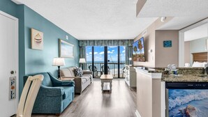 Un salon avec un canapé, une table basse et un téléviseur. Il y a un balcon avec vue sur l’océan.