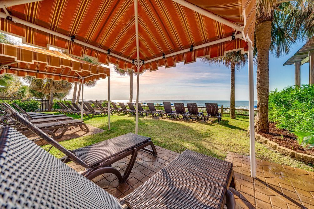 A covered outdoor seating area with lounge chairs and a view of the ocean.