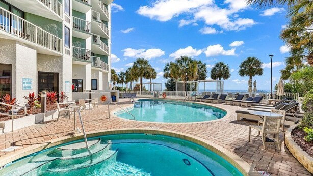 Un espace piscine avec des chaises longues et un bâtiment doté de balcons.