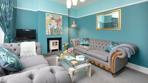 Ein Wohnzimmer mit türkisfarbenen Wänden, einem grauen Sofa, einem Glastisch und einem Kamin.