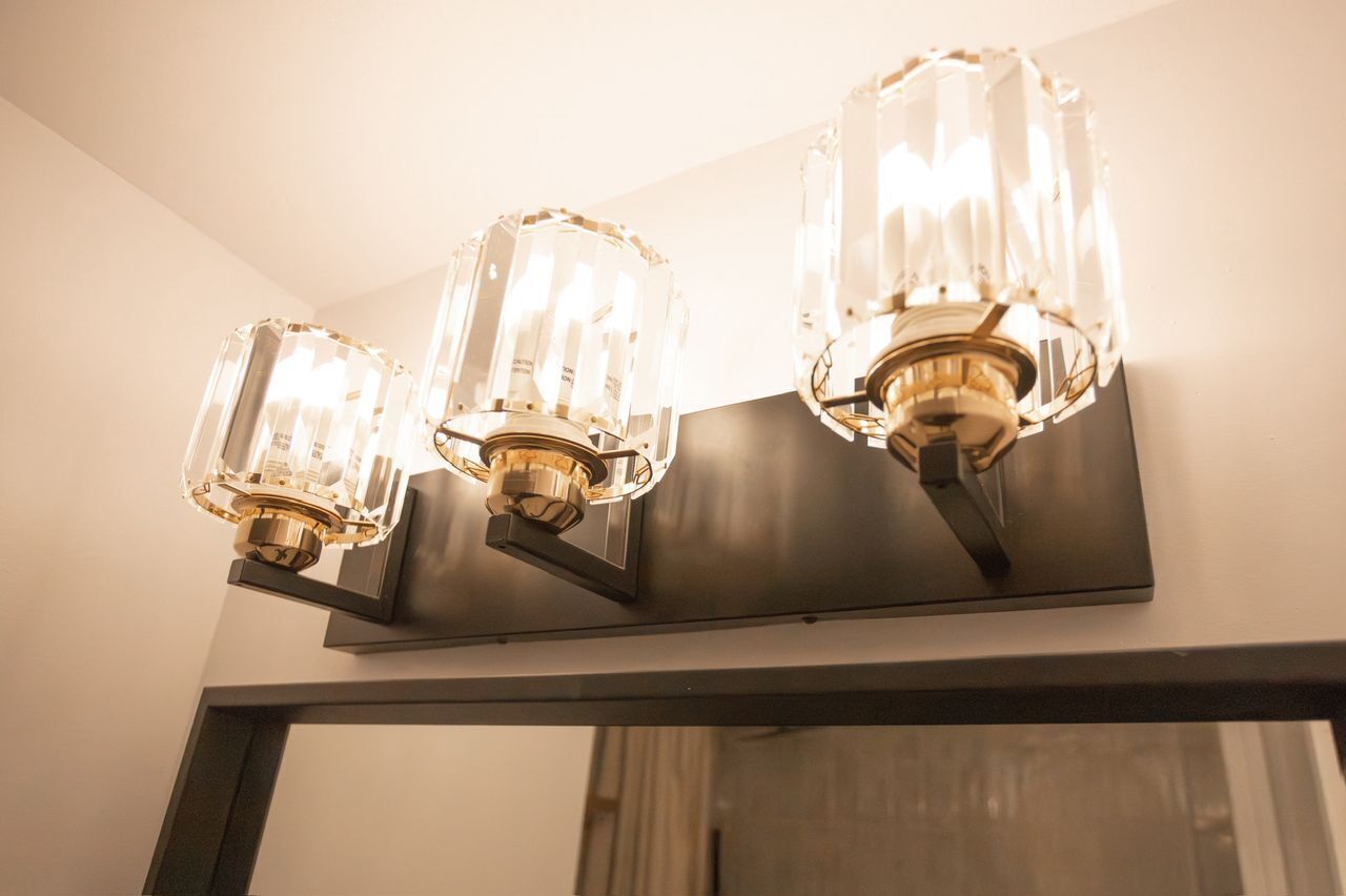 A wall-mounted light fixture with three clear glass shades and a gold-colored base.
