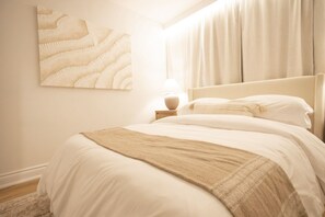 A bedroom with a bed, a nightstand, a lamp, and a wall-mounted artwork.
