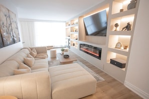 A modern living room with a sofa, TV, fireplace, shelves, and artwork.