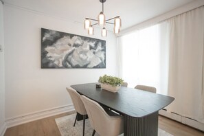 A modern dining room with a dark wooden table, beige chairs, a potted plant, and a large abstract painting on the wall.
