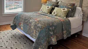 Ein Schlafzimmer mit Bett, Deckenventilator, Fenster mit Jalousien und einem gemusterten Teppich.