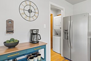 A kitchen with a modern stainless steel refrigerator, a coffee maker, a clock, and a bowl of green apples on a wooden countertop. - Walkable Downtown Sturgeon Bay - The Florist House (Sturgeon Bay)