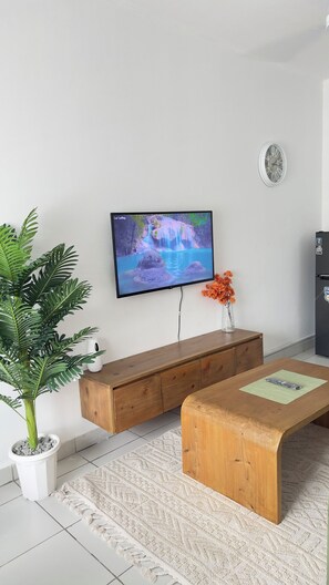 A living room with a flat-screen TV, wooden furniture, a potted plant, and a clock on the wall. - Olive wood apartment - Mombasa (Mombasa)
