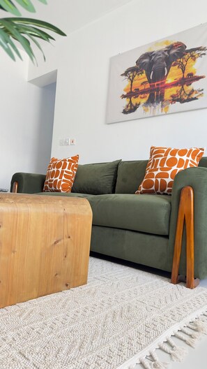 A green sofa with giraffe-patterned pillows, a wooden ottoman, and a white textured rug. - Olive wood apartment - Mombasa (Mombasa)