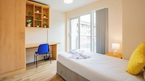 A hotel room with a bed, a desk, a chair, a wardrobe, a window, and a bedside lamp. - Modern 4 Bedroom Apartment In Limerick City (Limerick)