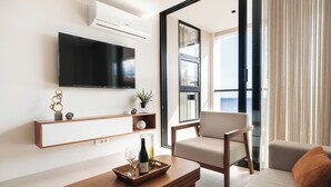 A modern living room with a flat-screen TV, a wooden coffee table with a wine bottle and glasses, a sofa, and a chair. - Bocobay Majestic Apartments (Willemstad)
