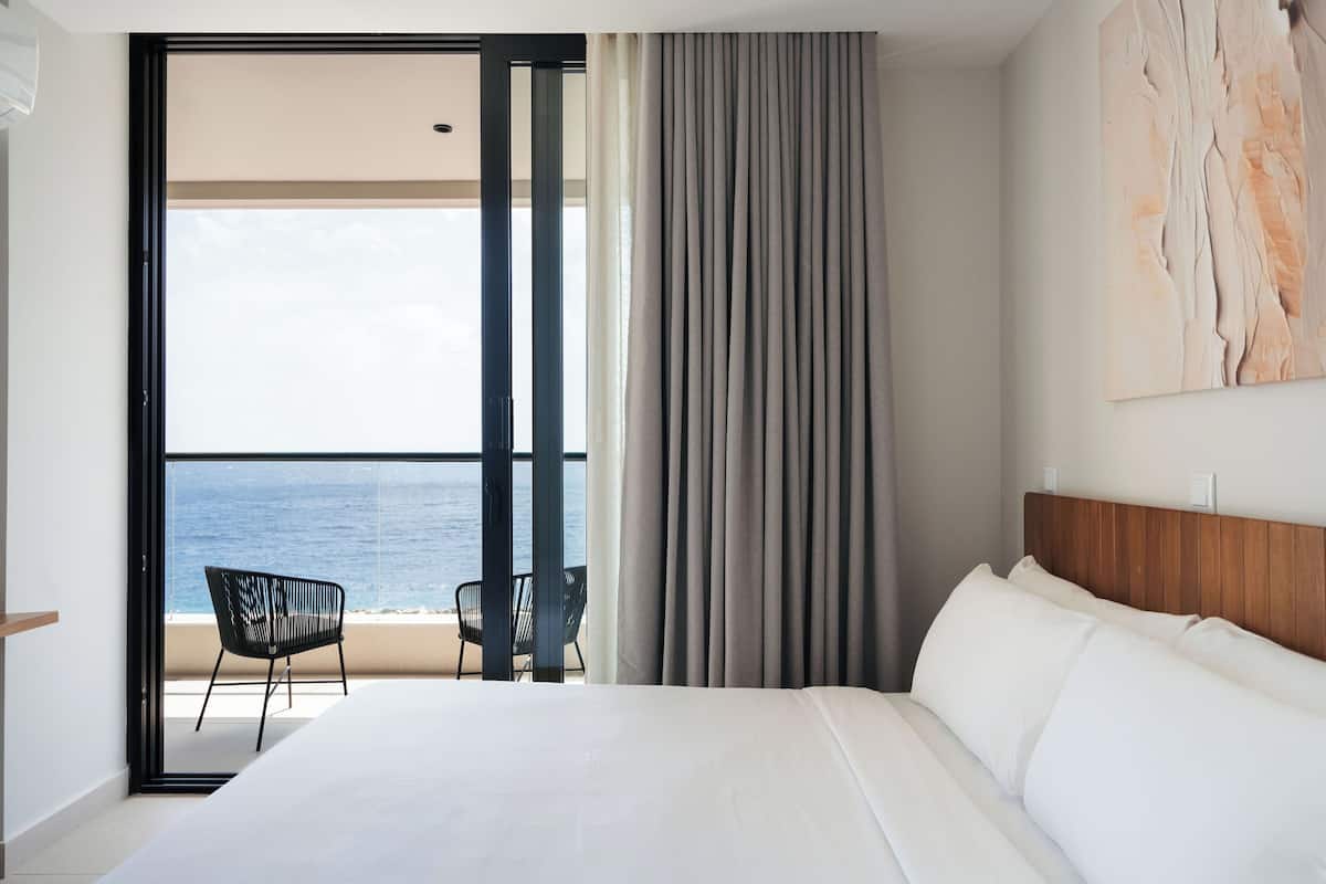 Une chambre d’hôtel avec un lit, une chaise, une vue sur l’océan et un grand tableau accroché au mur.