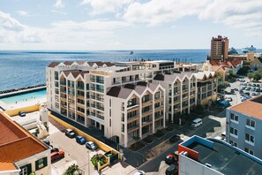 Un hôtel à plusieurs étages, doté de balcons, d’une piscine et offrant une vue sur la mer.