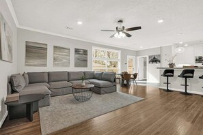 A modern living room with a sectional sofa, a coffee table, and a dining area with bar stools. - Luxury 4BR w Pool, Cinema & Game Room - 10pax (Houston)