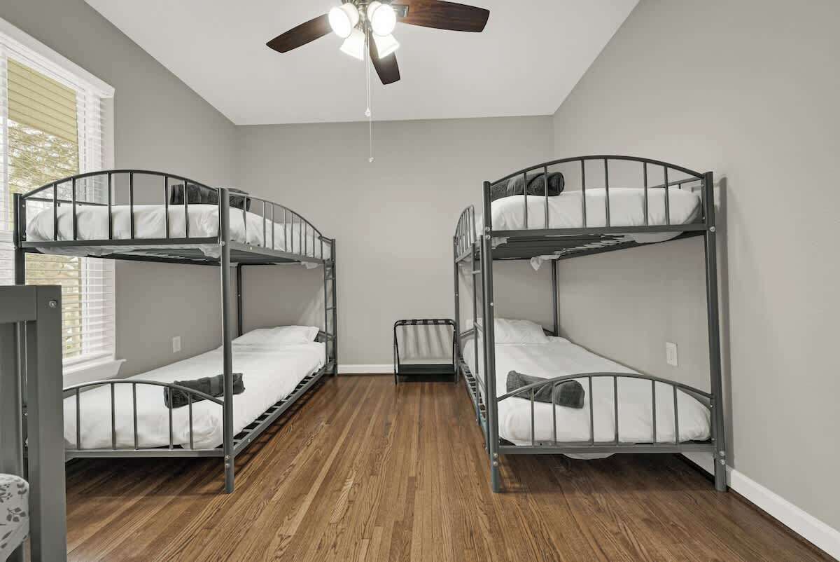 A room with two bunk beds, a ceiling fan, and a window with blinds.