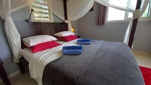 Una camera da letto con un letto, cuscini bianchi e rossi, asciugamani blu, una tenda a baldacchino e una finestra con tende.