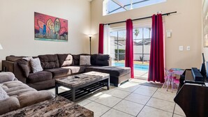 A living room with a sectional sofa, a coffee table, a piano, and a large window with red curtains. - 5BR Villa Private Pool & Game Room (Kissimmee)