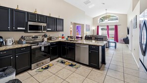 A modern kitchen with dark cabinetry, stainless steel appliances, and a large island. - 5BR Villa Private Pool & Game Room (Kissimmee)