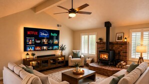 Ein Wohnzimmer mit Kamin, Fernseher, der Streamingdienste anzeigt, und Deckenventilator.