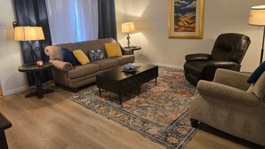 Un soggiorno con divano, poltrona, tavolino, due lampade, un tappeto e un quadro appeso alla parete.