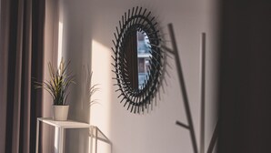 Une pièce avec une étagère blanche sur laquelle est posée une plante, un miroir fixé au mur et un lampadaire.