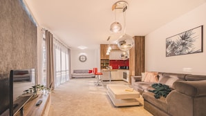 Un salon moderne avec un canapé, un fauteuil rouge, une table basse et, au fond, un coin cuisine.