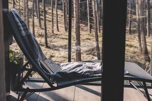 Ein Liegestuhl mit Decke, ein Topfpflanze und Blick auf einen Wald.