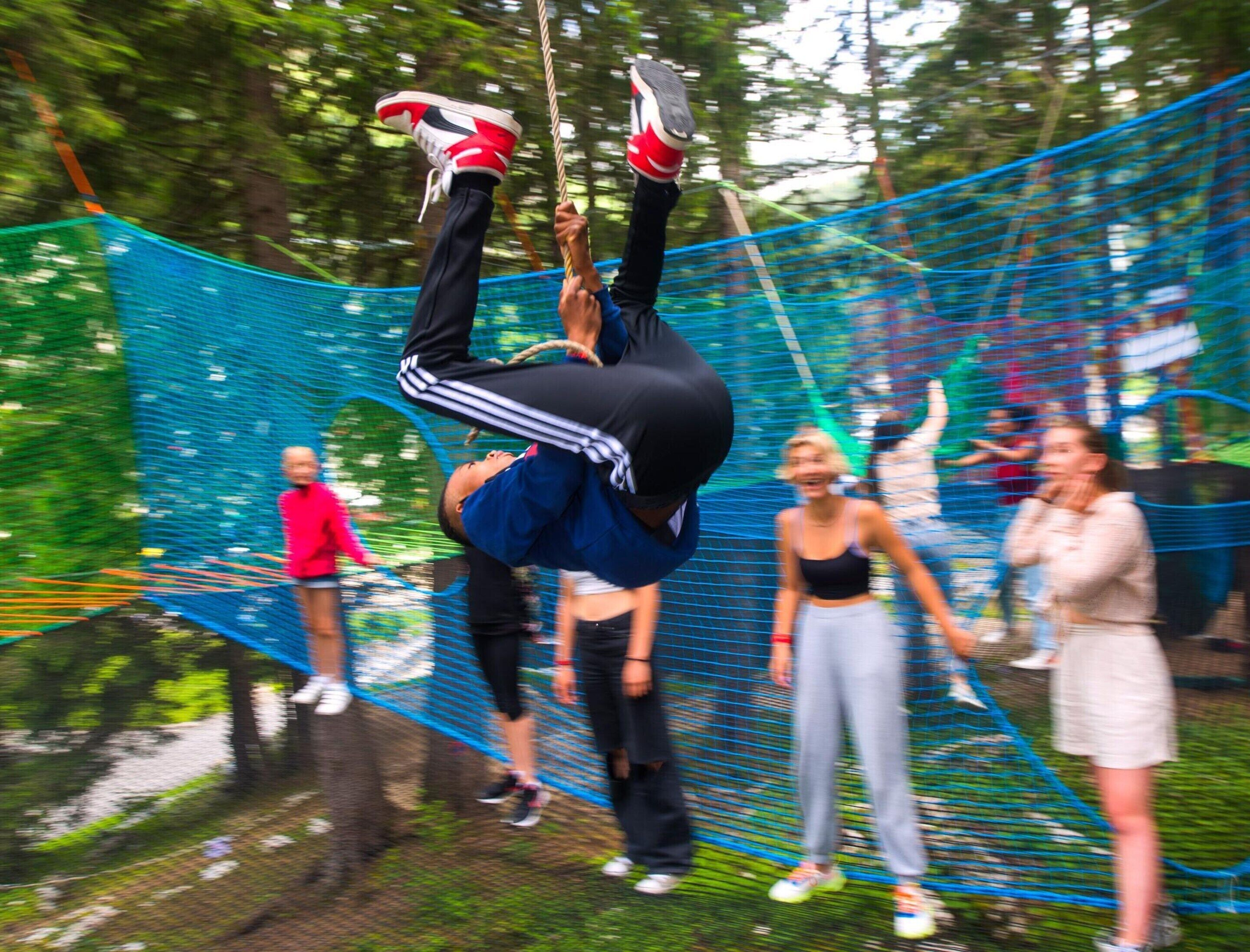 A person performing an acrobatic stunt on a blue net structure in an outdoor setting.