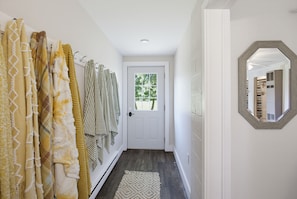 A hallway with a door, a mirror, and a rack of towels.