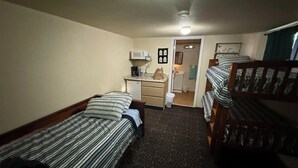 Una habitació amb dos llits individuals, un escriptori amb cadira, microones i una cuineta petita.