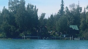 Una casa a la vora d'un llac amb un moll, envoltada d'arbres.