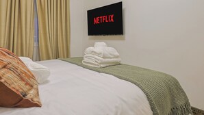 Ett hotellrum med en säng, en tv som är monterad på väggen och ett fönster med gardiner.
