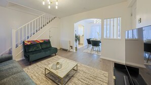 Ett vardagsrum med en trappa, en grön soffa, ett soffbord, en tv och en matplats med stolar och ett bord.