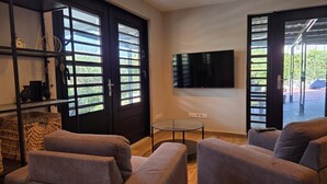 Ein Wohnzimmer mit Fernseher, zwei Sofas, einem Glastisch und einer Tür mit Fenstern.