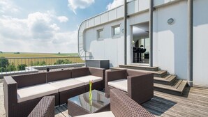 An outdoor deck with wicker furniture and a glass table, overlooking a field. - Hotel Bad Rappenau (Bad Rappenau)