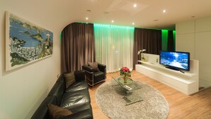 A modern living room with a leather sofa, a glass coffee table, a flat-screen TV, and a cityscape painting. - Hotel Bad Rappenau (Bad Rappenau)